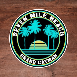 Puede incluir: Una pegatina circular negra y amarilla con el texto "Seven Mile Beach Grand Cayman" y un gráfico de palmeras y una puesta de sol.