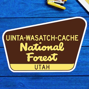 以下が含まれることがあります： 「ユインタ・ワサッチ・キャッシュ国立森林公園 ユタ州」と書かれた茶色と黄色の看板。