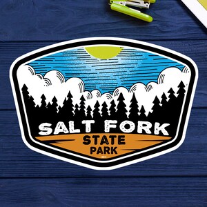 Puede incluir: Una pegatina azul y blanca con una escena de montaña y el texto "Salt Fork State Park".