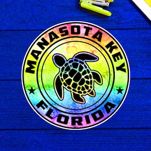 Puede incluir: Una pegatina circular de colores arcoíris con el texto "Manasota Key Florida" y una silueta negra de una tortuga marina en el centro.
