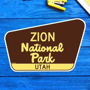 May include: A brown and yellow sign with the text "ZION National Park UTAH" on a blue wooden background.