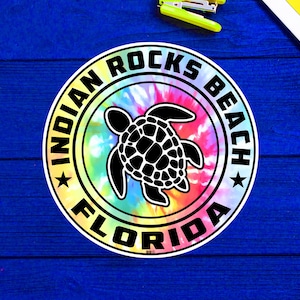May include: A round sticker with a tie-dye background and a black silhouette of a sea turtle. The sticker says "Indian Rocks Beach Florida" in a black circle around the turtle.