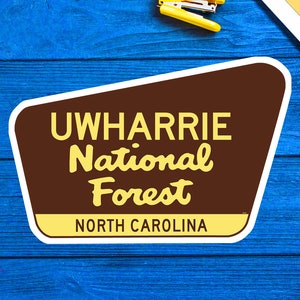 May include: A brown and yellow sign with the text "Uwharrie National Forest North Carolina".