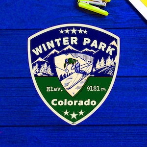 May include: A blue and green vintage-style sticker with the text "Winter Park, Colorado" and "Elev. 9121 ft."  The sticker features a skier in a blue and white ski suit, mountains, and pine trees.