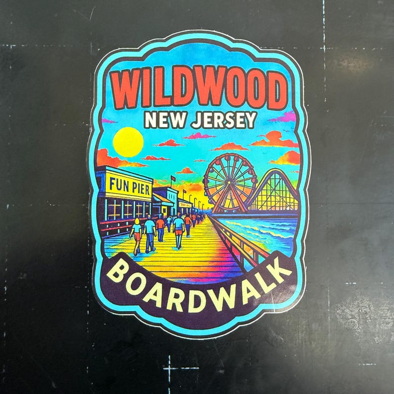 May include: A colorful sticker featuring the words "Wildwood New Jersey Boardwalk." The design includes a pier with people walking, a Ferris wheel, and a roller coaster, set against a vibrant sunset sky with a yellow sun.