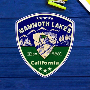 Puede incluir: Una pegatina de estilo vintage en forma de escudo, verde, azul y blanco con el texto "Mammoth Lakes, Elev. 7881, California" y un esquiador en las montañas.