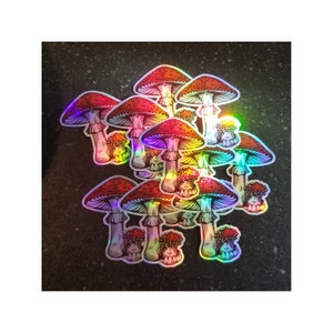 May include: A collection of holographic stickers featuring detailed illustrations of red and white spotted mushrooms. The stickers have a rainbow sheen, with vibrant colors and intricate line art, creating a whimsical and eye-catching design.