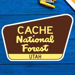 以下が含まれることがあります： レトロなフォントで「CACHE National Forest UTAH」と書かれた茶色と黄色の看板です。