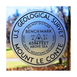 May include: A silver round sticker with black text that reads "U.S. Geological Survey" and "Mount Le Conte". The sticker also includes the text "Do Not Disturb", "Bench Mark", "Great Smoky Mountains National Park", "T + N", "6594 Feet Above Sea".