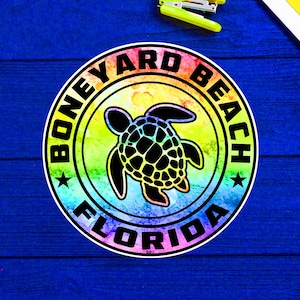 Peut inclure: Un autocollant rond avec un fond aquarelle arc-en-ciel et une silhouette noire de tortue de mer. L'autocollant dit "Boneyard Beach Florida" dans un cercle noir autour de la tortue.