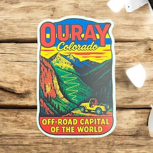 May include: A colourful sticker featuring the text "OURAY Colorado" in red and yellow. The sticker depicts a mountain landscape with a yellow jeep and the text "OFF-ROAD CAPITAL OF THE WORLD."