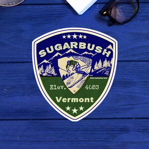 May include: A vintage-style sticker featuring a skier on a mountain slope with the text "Sugarbush" and "Vermont" in a white oval with a green border. The sticker also includes the text "Elev. 4083" and three stars.