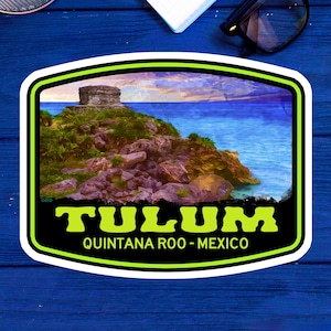 May include: A green and black sticker featuring a colourful image of a Mayan ruin on a cliff overlooking the ocean. The text "TULUM" is in green letters with the words "QUINTANA ROO - MEXICO" in smaller white letters below.
