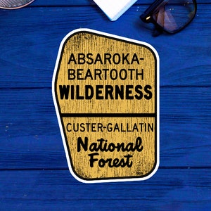 May include: A yellow and brown sticker with the text "Absaroka-Beartooth Wilderness Custer-Gallatin National Forest".