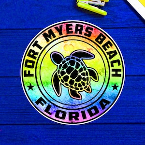 Puede incluir: Una pegatina circular de colores arcoíris con el texto "FORT MYERS BEACH FLORIDA" y una silueta negra de una tortuga marina en el centro.