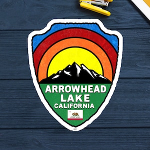 Könnte beinhalten: Ein bunter Aufkleber mit einem Retro-Design, das eine Bergkette, eine Sonne und den Text "Arrowhead Lake California" zeigt. Der Aufkleber enthält auch ein kleines Bild der Flagge des US-Bundesstaates Kalifornien.