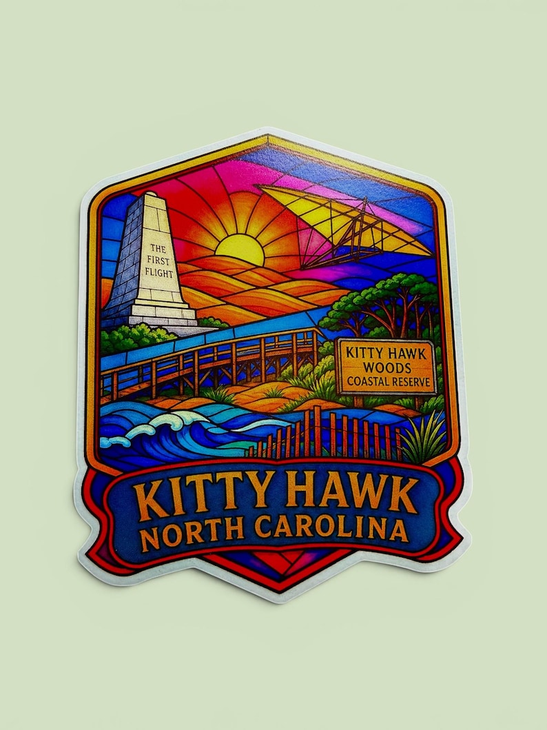 May include: A colorful sticker featuring a stained-glass style illustration of Kitty Hawk, North Carolina. It depicts the Wright Brothers monument with the text The First Flight, a glider, a wooden boardwalk, and a sign reading Kitty Hawk Woods Coastal Reserve.