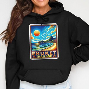 May include: Black hoodie with a colorful graphic of a beach scene in Phuket, Thailand. The graphic features a sunset, ocean waves, and a mountain range. The text "Phuket Thailand" is printed below the graphic.