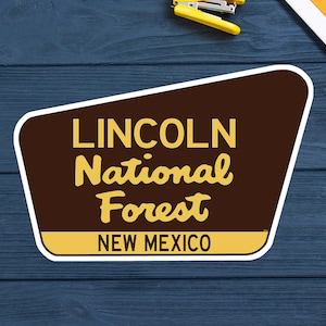 May include: A brown and yellow sign with white trim that reads "LINCOLN National Forest NEW MEXICO".
