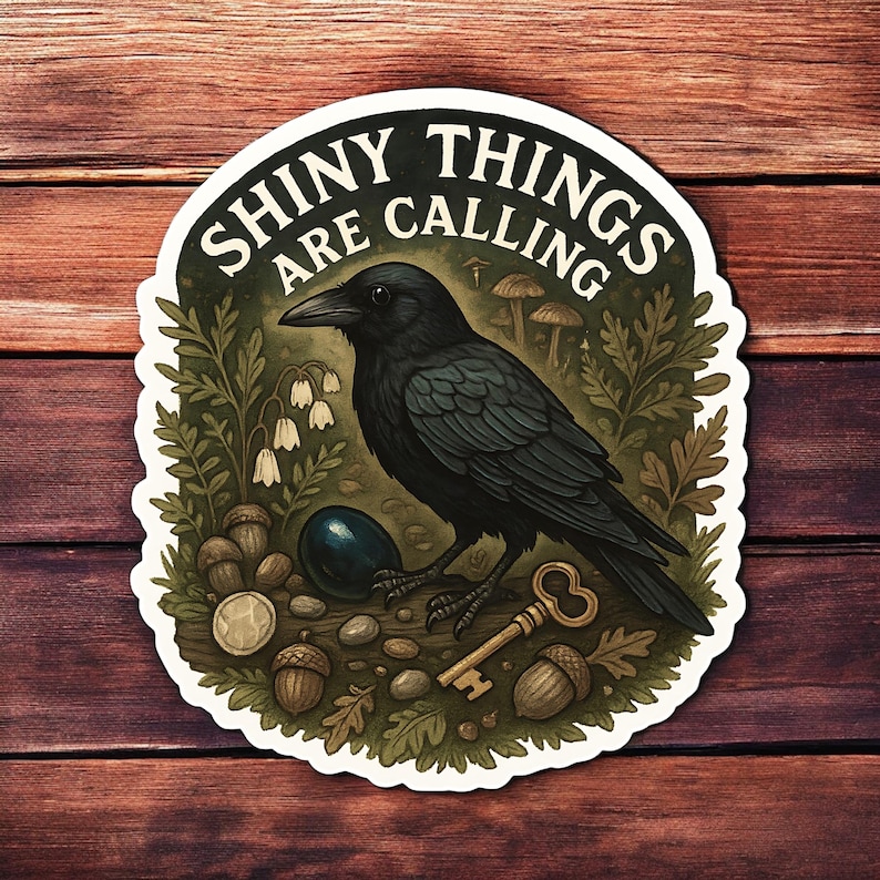 Puede incluir: Una pegatina con un cuervo negro y el texto "Shiny Things Are Calling". El cuervo est&aacute; rodeado de bellotas, una llave y otros elementos naturales. La pegatina tiene un borde blanco y est&aacute; sobre un fondo de madera.