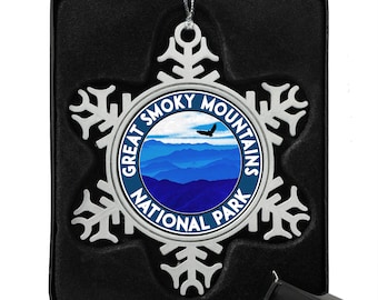 May include: Silver snowflake ornament with a blue and white image of the Great Smoky Mountains National Park logo. The ornament is in a black velvet box.