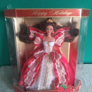 May include: A Special Edition Barbie doll in a box. The doll is wearing a red and white gown with gold accents. The box reads "Happy Holidays" and "Barbie". The doll has brown hair and is wearing a tiara.
