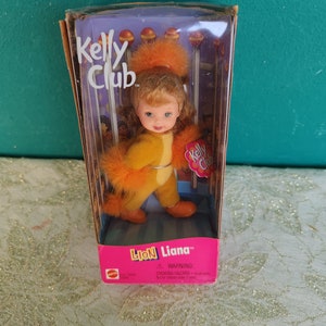 May include: A Kelly Club Liana doll in a box. The doll is dressed in a yellow and orange lion costume. The box has the words "Kelly Club" and "Lion Liana" printed on it.