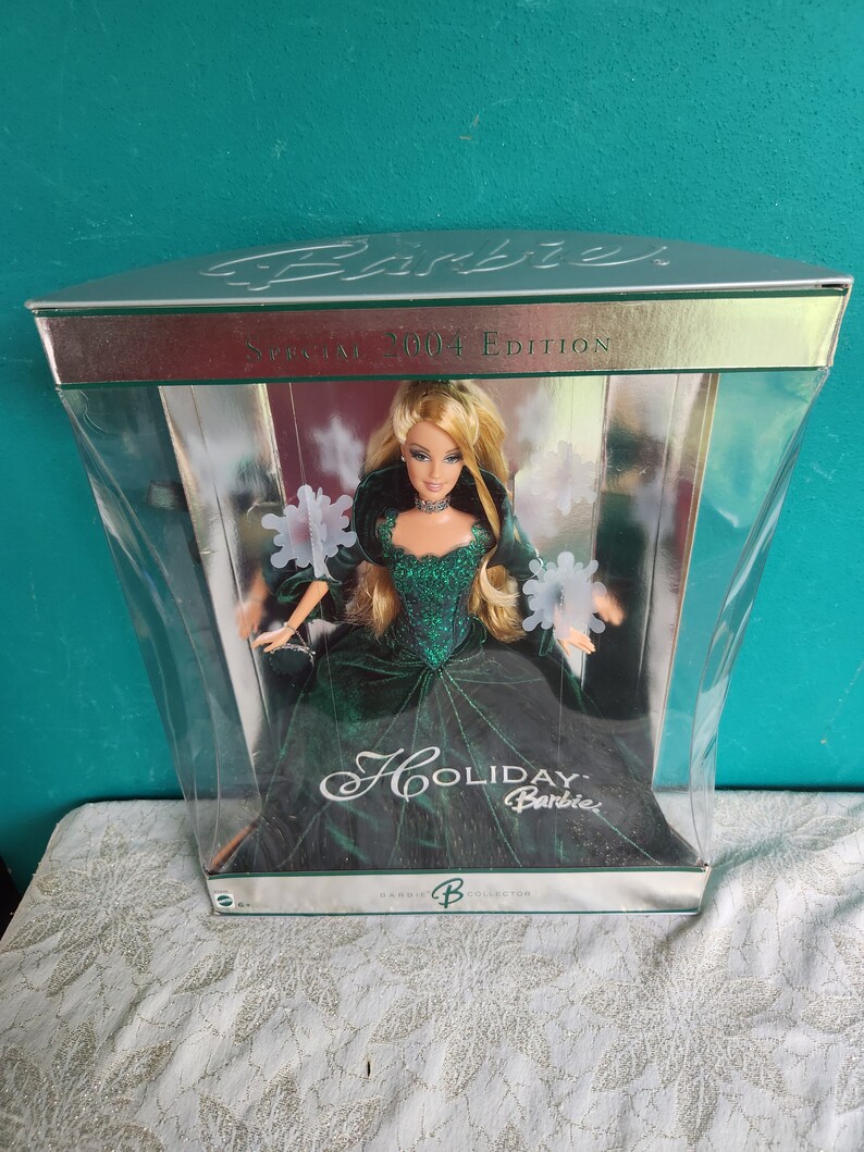 May include: 2004 Holiday Barbie Collector Edition doll in a clear plastic display case. The doll wears a sparkling emerald green gown and has blonde hair. The box features silver accents and the text 'Barbie', 'Special 2004 Edition', and 'Holiday Barbie'.
