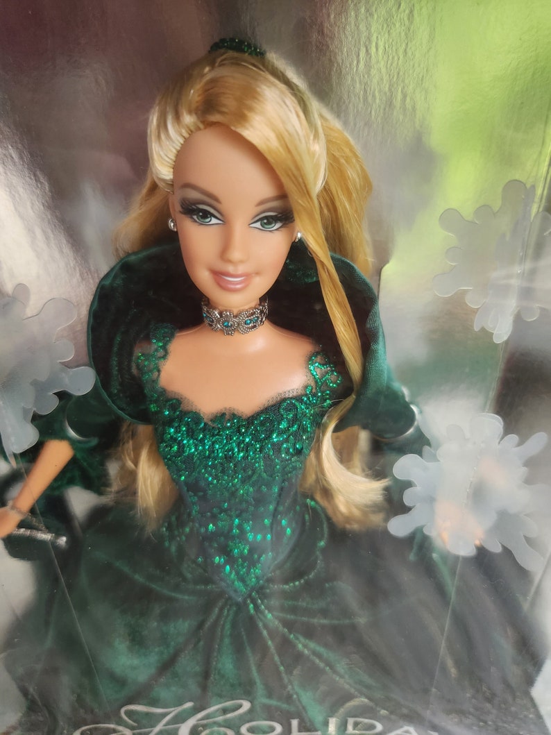 May include: Barbie Holiday 2006 doll in a dark green velvet gown, adorned with sparkling emerald accents.  Her blonde hair is styled elegantly, and she wears a silver necklace. The packaging features snowflake designs.
