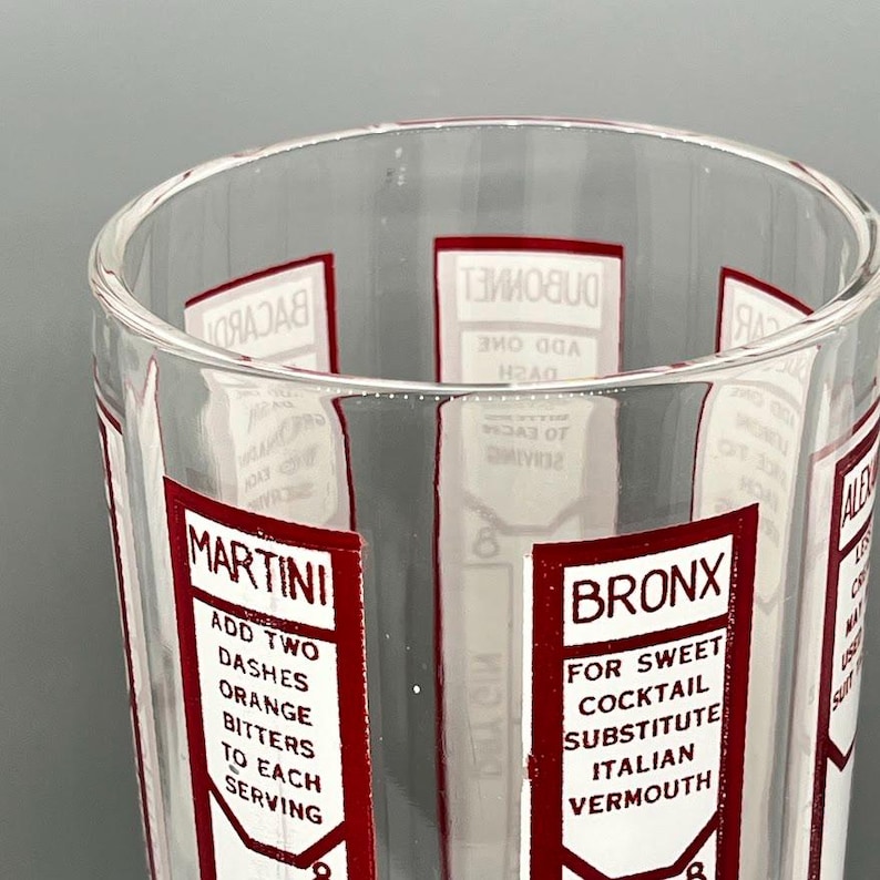 Peut inclure: Un verre doseur en verre transparent avec des &eacute;tiquettes rouges et blanches pour diff&eacute;rents cocktails. Les &eacute;tiquettes comprennent des instructions pour faire un Martini, un Bronx et d'autres boissons. Les &eacute;tiquettes comportent des textes tels que "Ajouter deux traits d'amertume d'orange &agrave; chaque service" et "Pour un cocktail sucr&eacute;, remplacer par du vermouth italien".