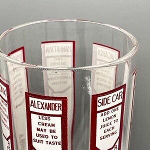 Peut inclure: Un verre doseur en verre transparent avec des &eacute;tiquettes rouges et blanches listant diff&eacute;rentes recettes de cocktails, dont "Manhattan", "Alexander", "Side Car" et "Bacardi".