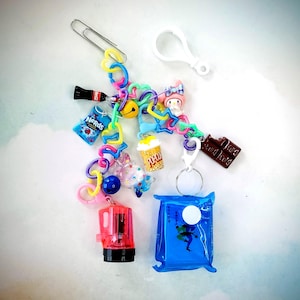 May include: A colorful charm bracelet with various charms, including a soda can, a popcorn bucket, a chocolate bar, a Hello Kitty character, and a blue pouch with a white circle.