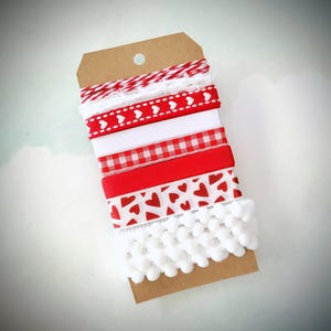 May include: A collection of decorative ribbons in red, white, and a red and white pattern, attached to a brown tag. The ribbons include various designs, such as hearts, gingham, and pom-poms, perfect for crafting and gift wrapping.