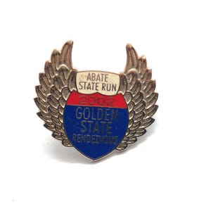 May include: A vintage pin with a shield design and stylized wings. The pin features the text "ABATE STATE RUN" at the top, "2002" in the middle, and "GOLDEN STATE RENDEZVOUS" at the bottom. The shield has red and blue sections.