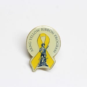 May include: A yellow ribbon pin with the words "ARNG YELLOW RIBBON PROGRAM" around the ribbon. A blue silhouette of a person holding a rifle is in the centre of the ribbon.