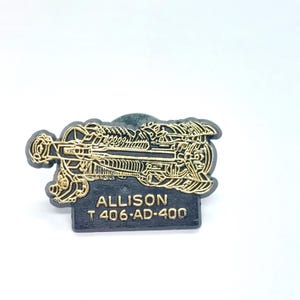 May include: A black and gold Allison T 406-AD-400 pin. The pin features a detailed, gold-colored mechanical design on a black background. The text "ALLISON" and "T 406-AD-400" are visible on the pin.