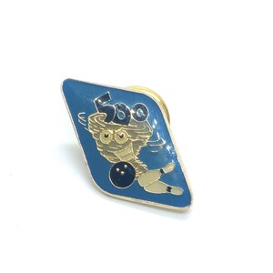 May include: A blue diamond-shaped pin with a gold outline. The pin features a cartoon bowling pin with a bowling ball and the number 500.