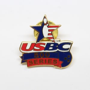 May include: A gold-coloured pin with a blue, white and red star featuring a bowling pin inside. The star is above the text "USBC 500 SERIES" in blue, white and red lettering. The pin has a blue bowling ball with three white dots on it.