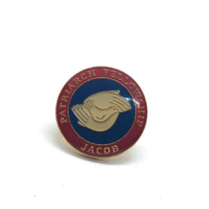 May include: A round pin with a red border and the words "PATRIARCH FELLOWSHIP" in white. The center has a blue background with two tan hands holding a tan dove. The word "JACOB" is at the bottom.