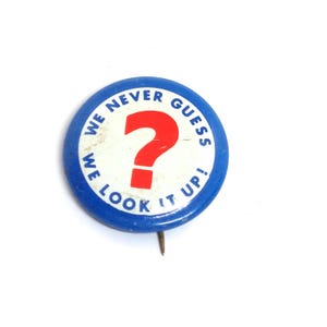 May include: A round blue button with the text "WE NEVER GUESS WE LOOK IT UP!" encircling a white center with a red question mark. The button has a pin on the back.