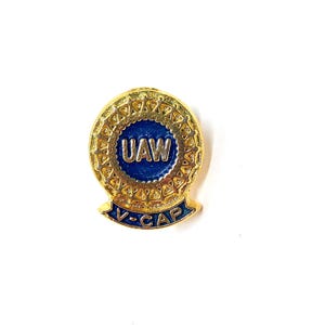 May include: Gold pin with a blue circle containing the letters UAW and a gold banner with the text V-CAP.