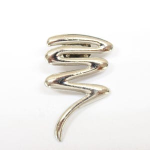 May include: Silver-toned abstract swirl pin. The pin is made of metal and has a wavy, abstract design. It is a simple and elegant piece of jewelry.