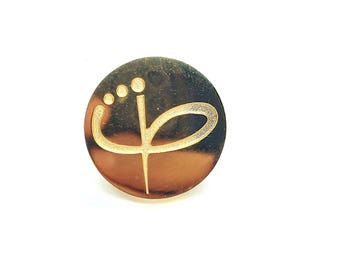May include: A gold-colored round pin with a stylized flower design in white.