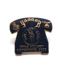 May include: A black and gold pin shaped like a telephone receiver. The pin features the word "YaararB" in gold lettering, along with the text "Mike Hulsey Potentate 2002" and a small illustration of a person.