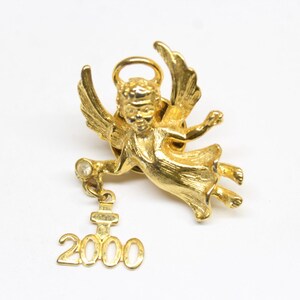 May include: Gold-tone angel pin with a dangling charm that reads "2000". The angel has wings, a halo, and a single rhinestone.