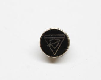 May include: A black and silver pin with a shield and sword design inside a triangle.