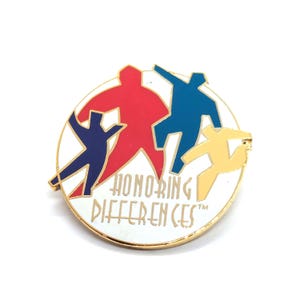 May include: A round pin with a gold border and the words "HONORING DIFFERENCES" in white. The pin features four stylized figures in red, blue, and yellow on a white background.