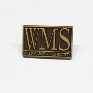 May include: A gold-coloured metal pin with the letters "WMS" in raised lettering on a brown background. The text "William McKendree Society" is printed below the letters.
