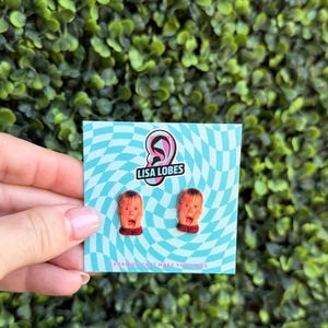 Pu&ograve; includere: Orecchini originali con un design a forma di volto che urla. Sono presentati su una carta a motivi blu e bianchi con il testo "LISA LOBES" e "EARRINGS THAT MAKE YOU SMILE".