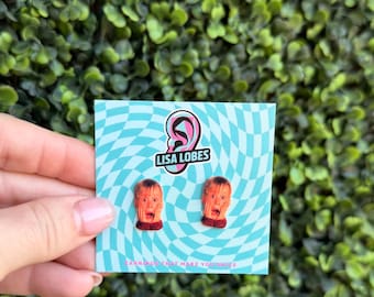 May include: A pair of novelty earrings featuring a screaming face design. The earrings are displayed on a blue and white patterned card with the text "LISA LOBES" and "EARRINGS THAT MAKE YOU SMILE".